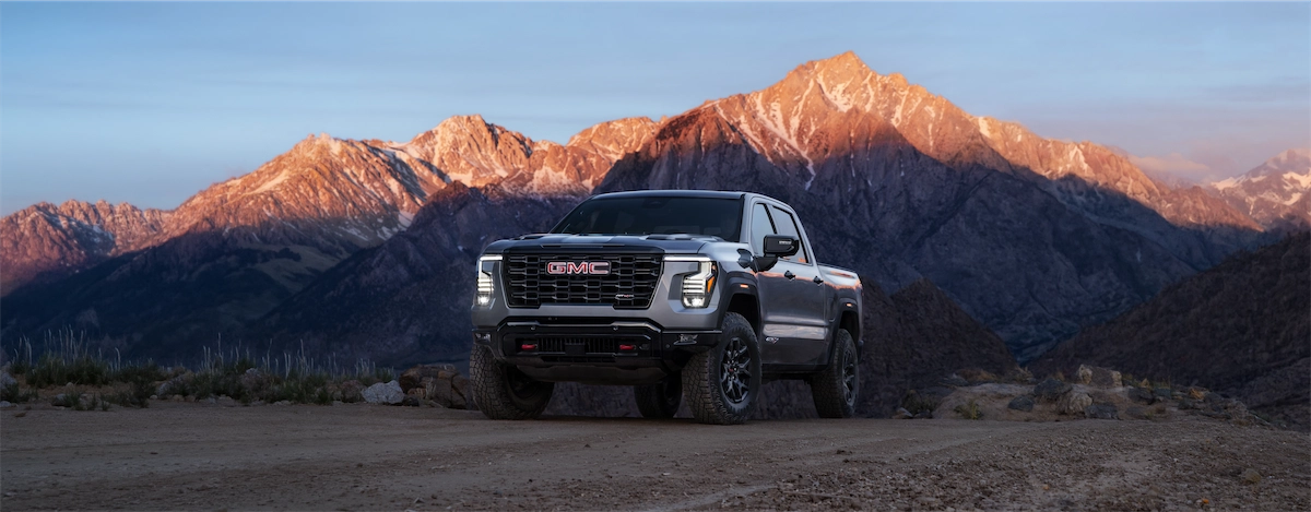 2027 GMC Sierra AT4X parked on a dirt trail in front of mountains at sunset