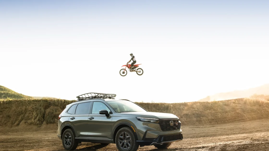 2026 Honda CR-V TrailSport parked on a dirt hill as a Honda dirt bike jumps overhead
