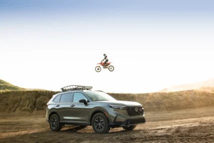 2026 Honda CR-V TrailSport parked on a dirt hill as a Honda dirt bike jumps overhead