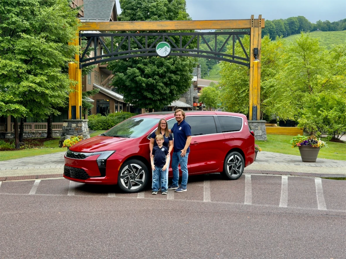 Family standing in front of a red 2027 Chrysler Pacifica Limited AWD under a wooden archway