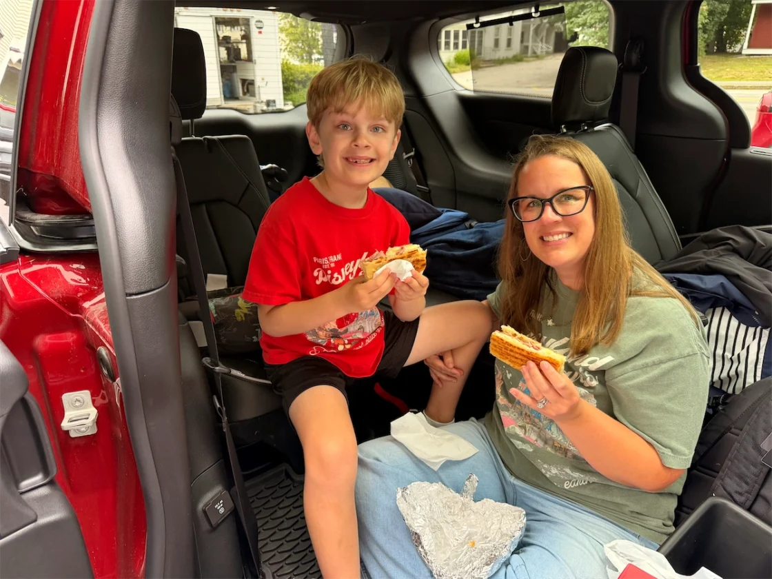 Boy and woman eating in the open second-row doorway of a 2027 Chrysler Pacifica