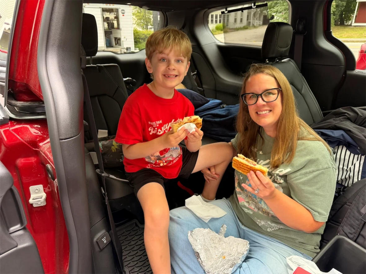 Boy and woman eating in the open second-row doorway of a 2027 Chrysler Pacifica