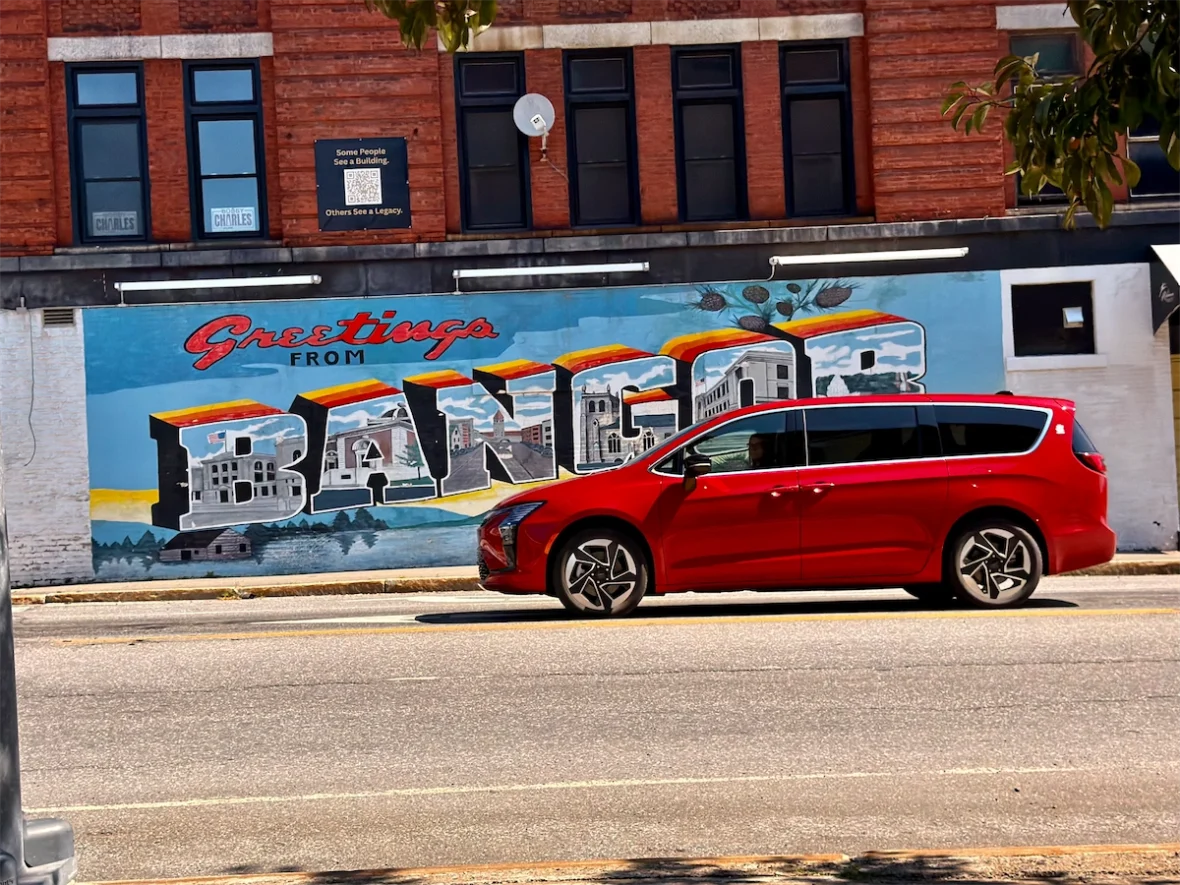 Red 2027 Chrysler Pacifica in profile beside a Greetings from Bangor mural in Maine