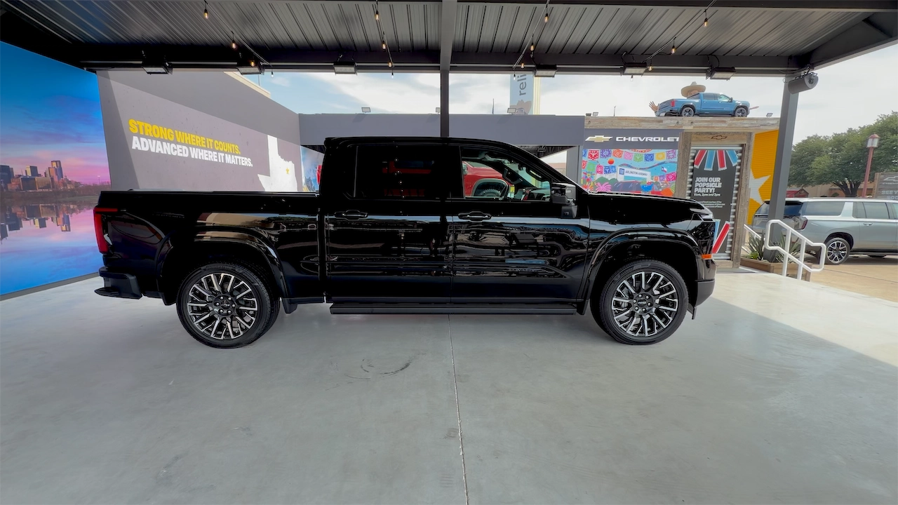 A black pickup truck displayed in an automotive showroom, featuring a sleek design and stylish wheels, with a colorful backdrop featuring promotional graphics.
