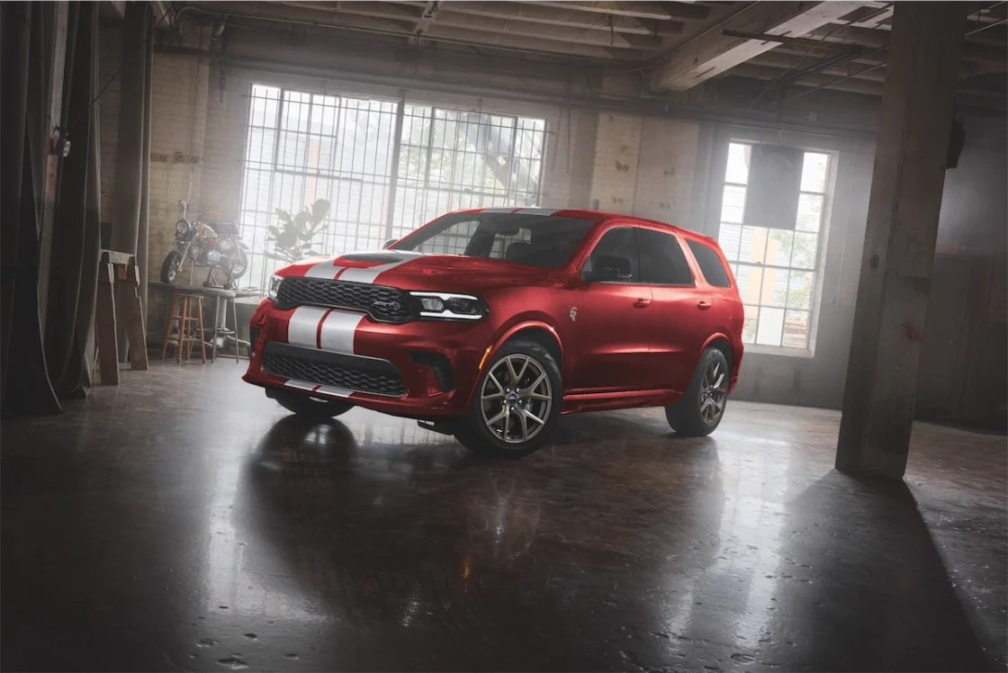 A red SUV with white racing stripes parked in an industrial setting, featuring large wheels and a sporty design.