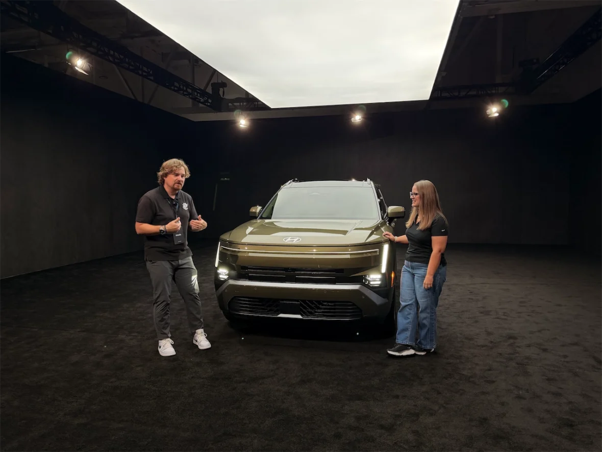 A presentation featuring a man and woman beside a green SUV in a spotlighted display area with a dark background.