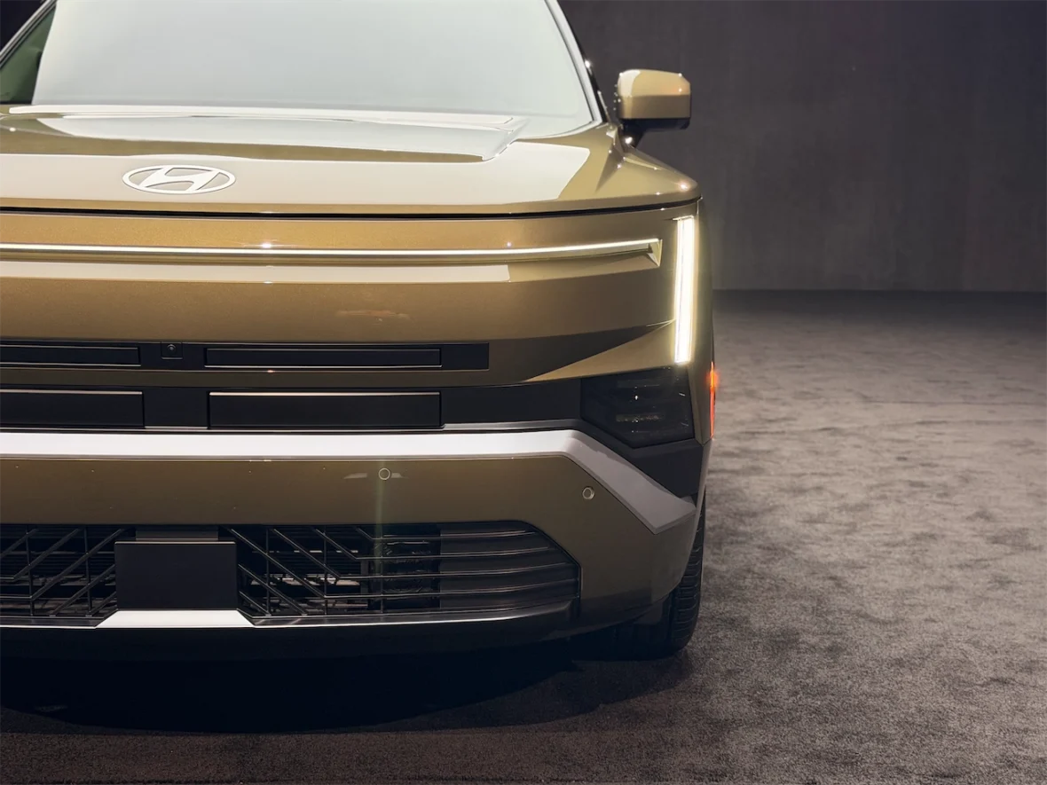 Close-up view of a modern car front, showcasing the sleek design and distinctive headlights, with a prominent logo on the hood.