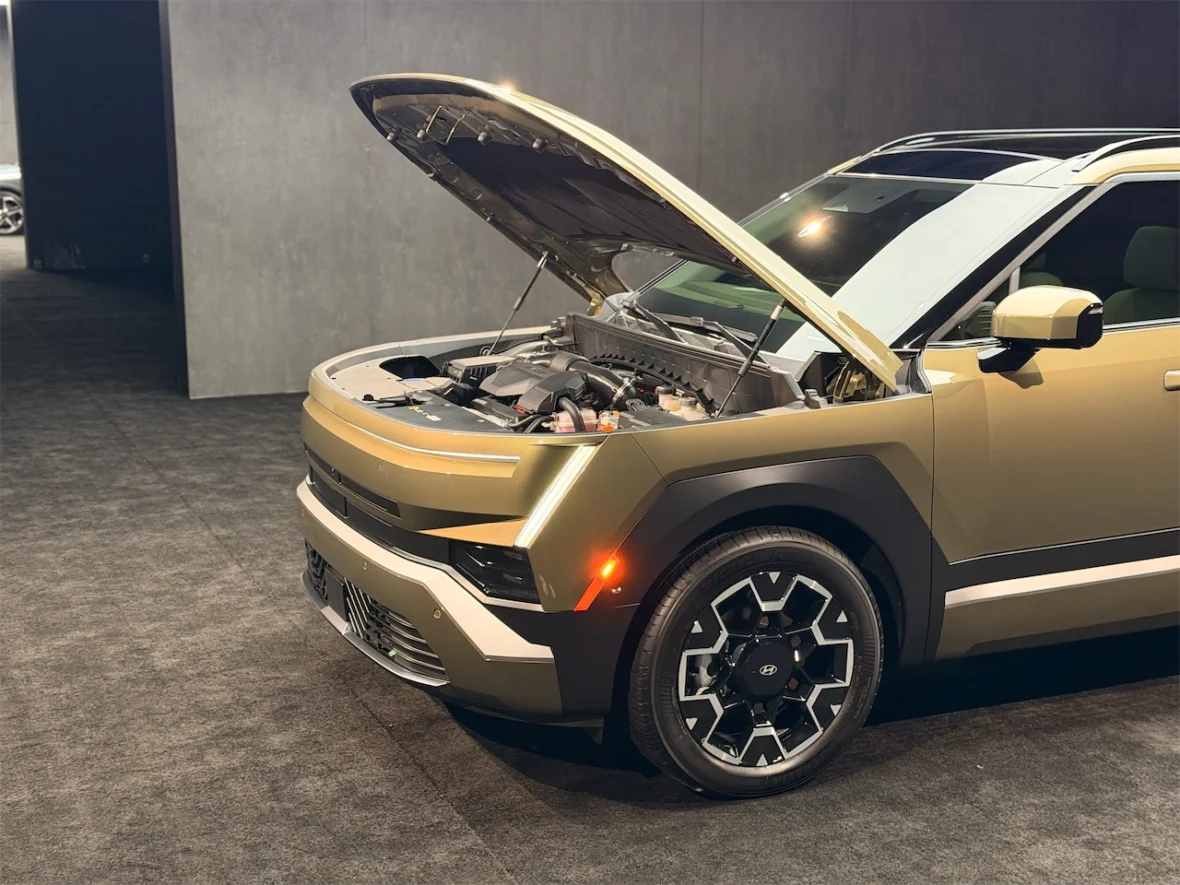 A close-up view of a stylish SUV with the hood raised, showcasing the engine compartment, set against a modern backdrop.