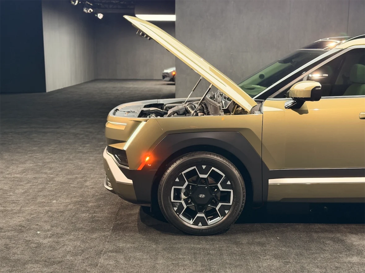 Side view of a car with the hood open, showcasing the engine, situated in a dimly lit exhibition space.