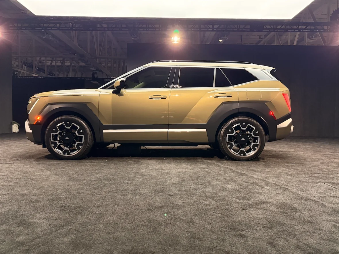 Side view of a modern SUV in a gold and black color scheme, showcased on a stage with soft lighting.