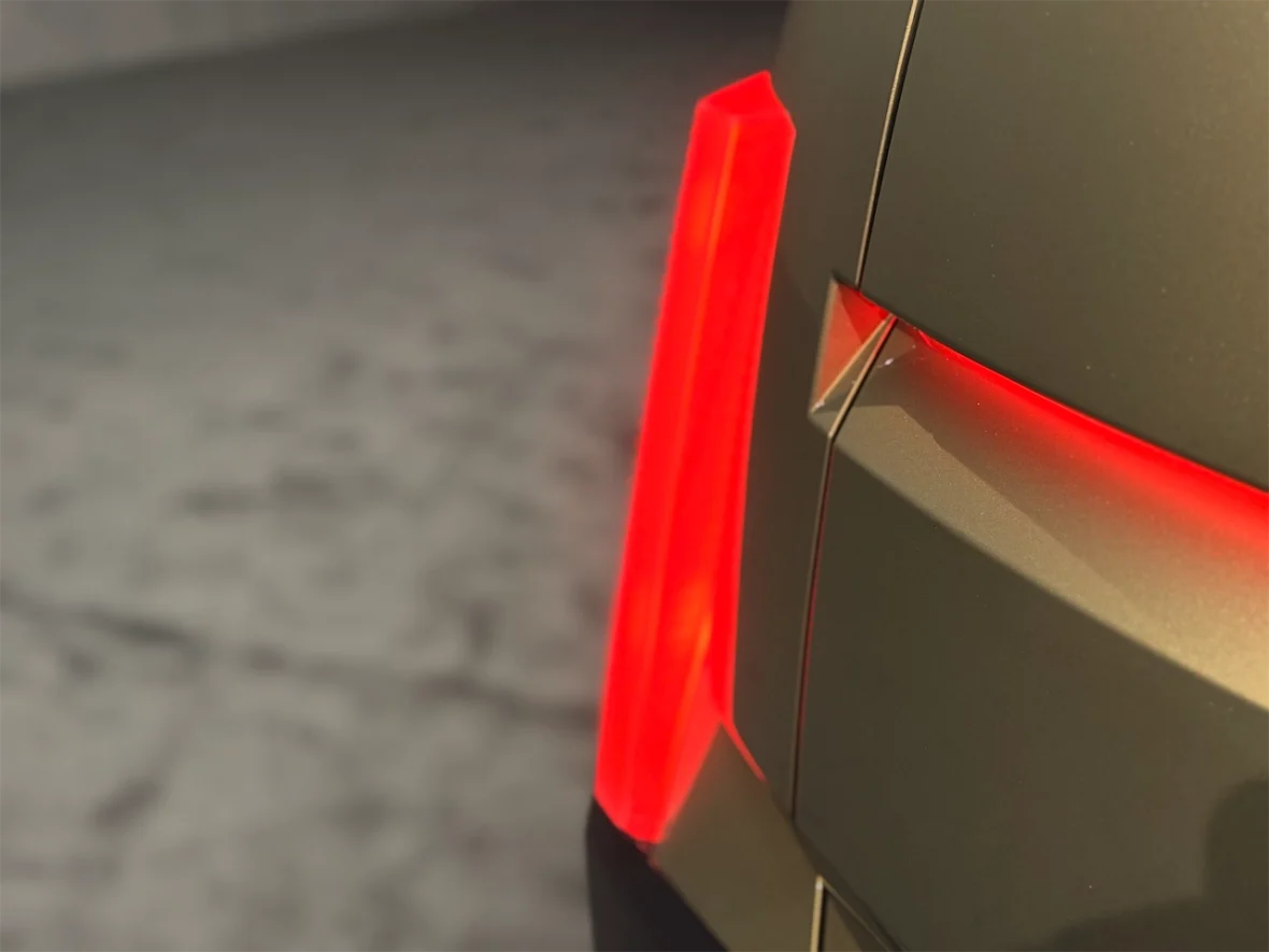 Close-up of a car's rear light with a glowing red accent on a sleek, metallic surface.