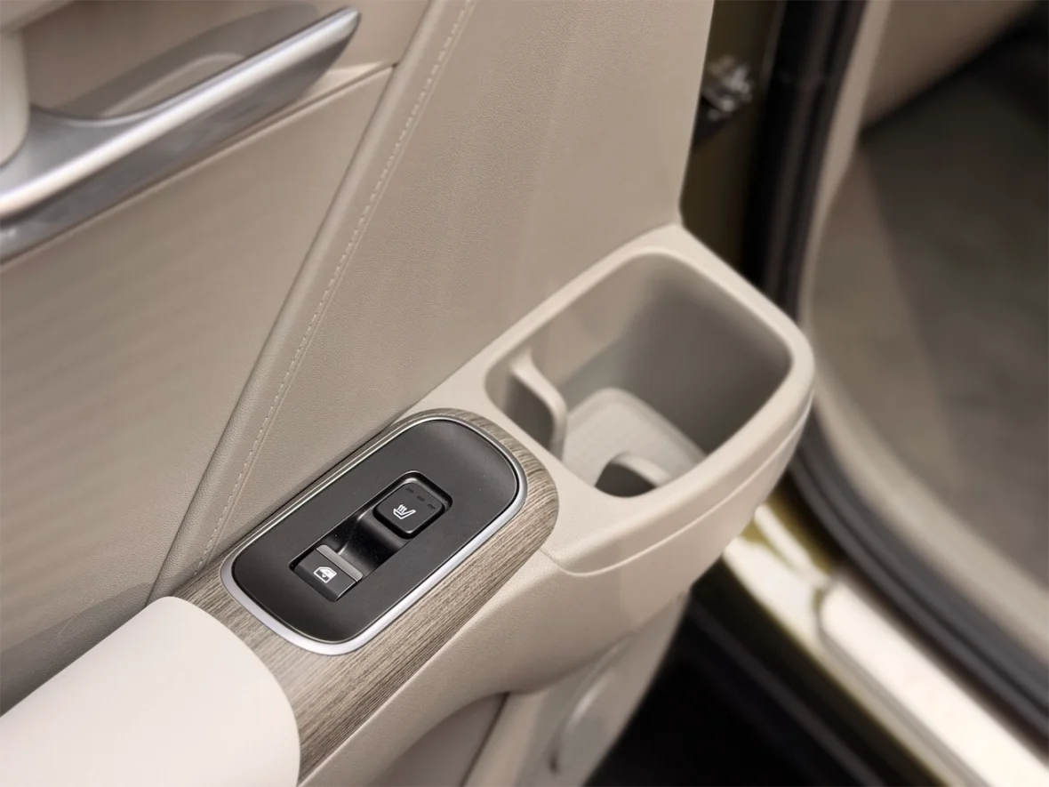 Close-up of a car door panel showing window control buttons and a cup holder, featuring a beige interior design.