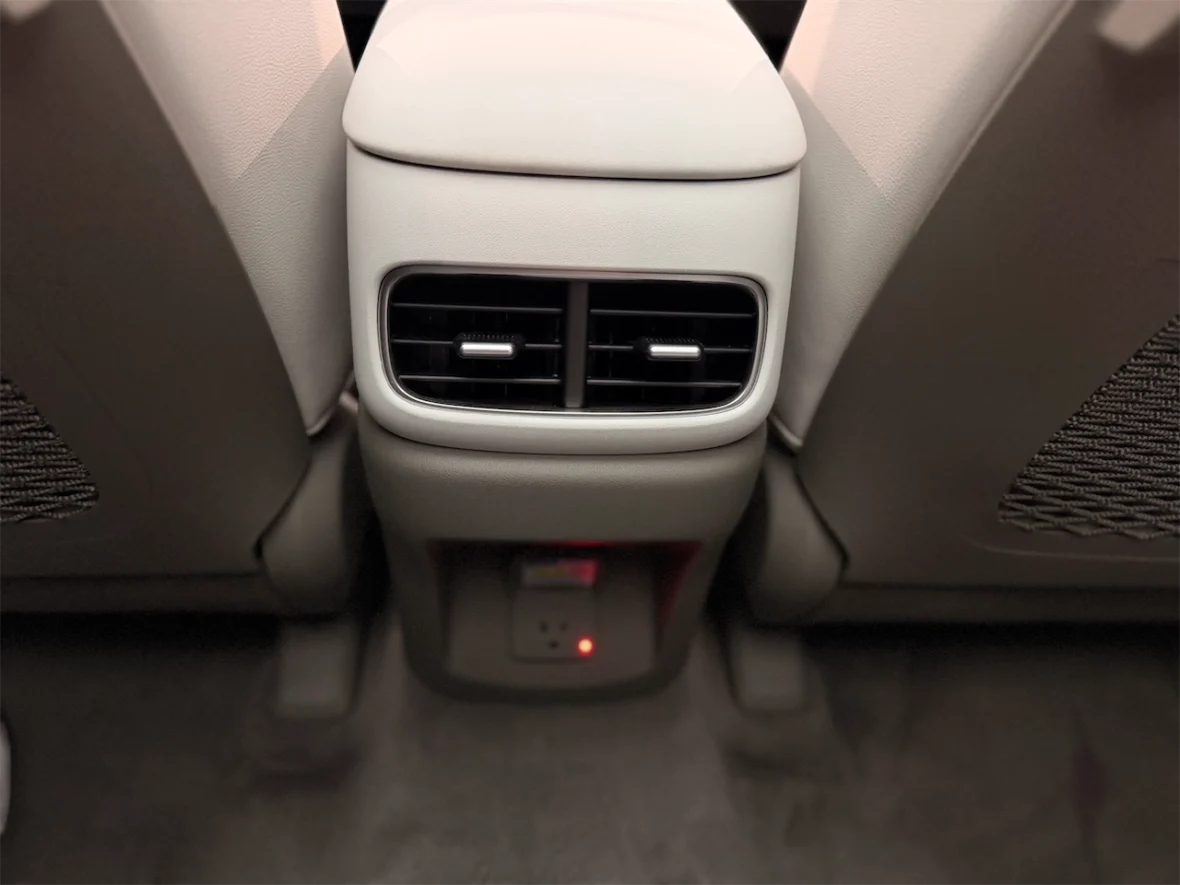 Close-up view of a car's rear center console featuring air conditioning vents and a power outlet.