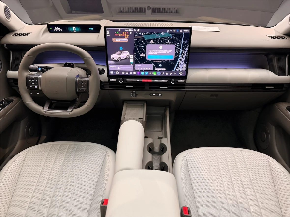 Interior view of a modern car showing a steering wheel, a large digital display with navigation and information, and comfortable seating in light-colored upholstery.