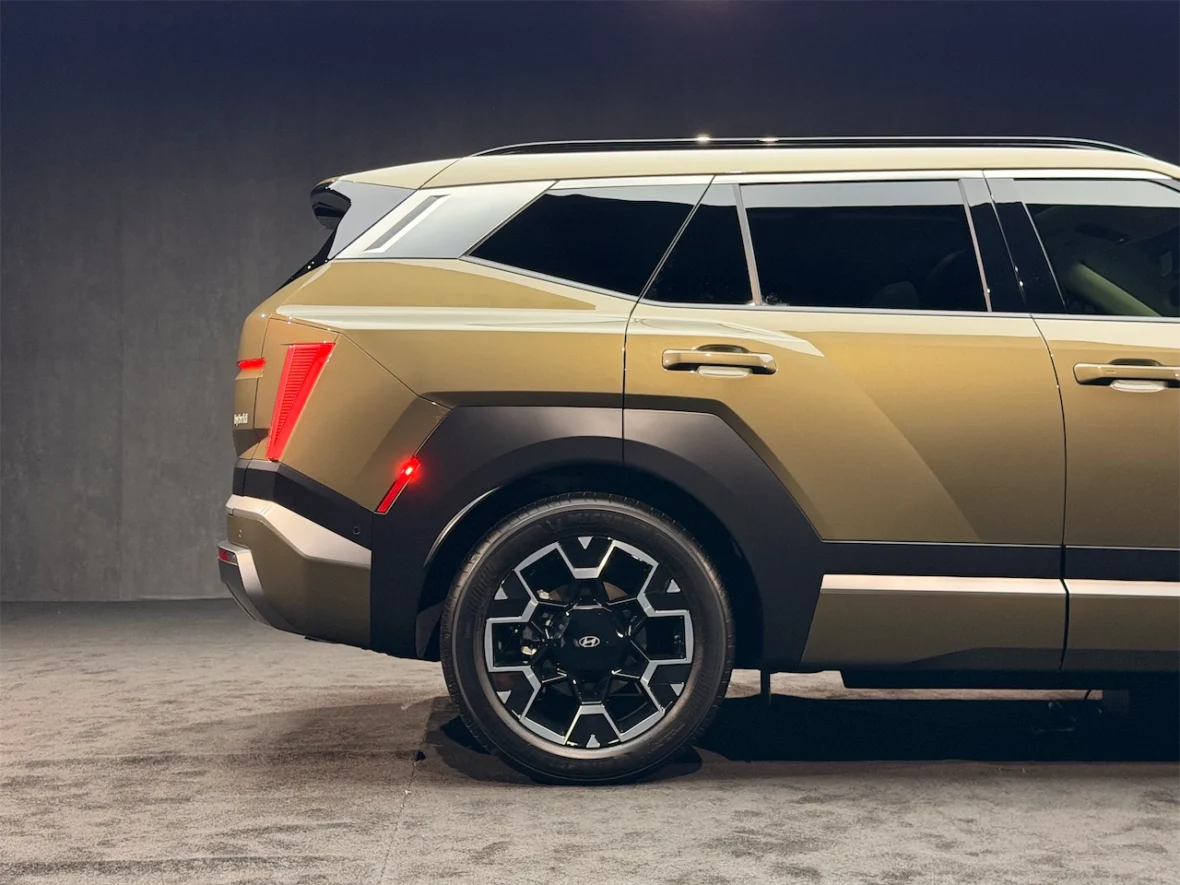 Side view of a modern SUV with a sleek design, featuring a greenish-gold paint and unique geometric wheel rims.