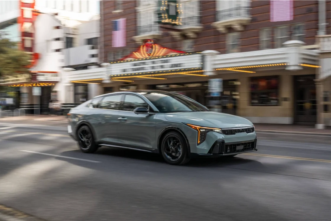 Gray Kia K4 sedan driving past a historic theater