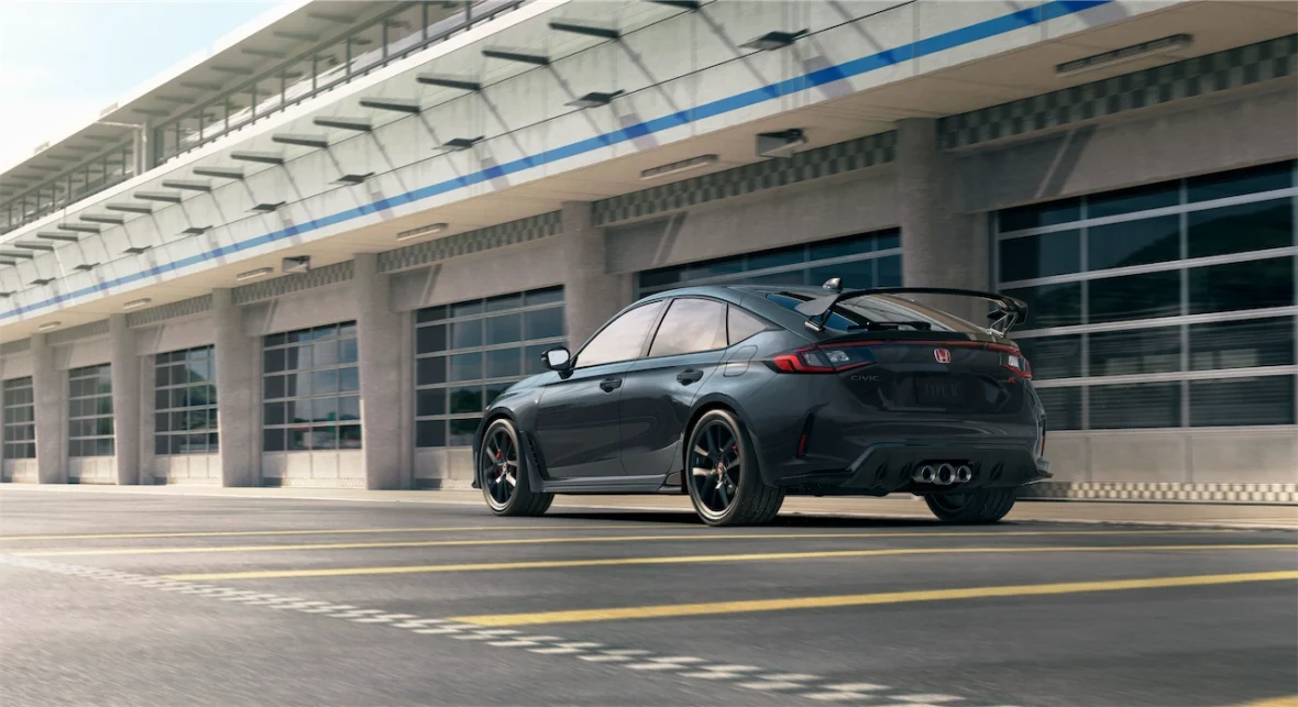Civic Type R rolling past the pit garages, showing its rear wing and triple exhaust