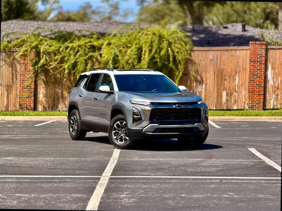 A silver SUV parked in a spacious lot, featuring a sleek design and modern styling, with a backdrop of greenery and a wooden fence.