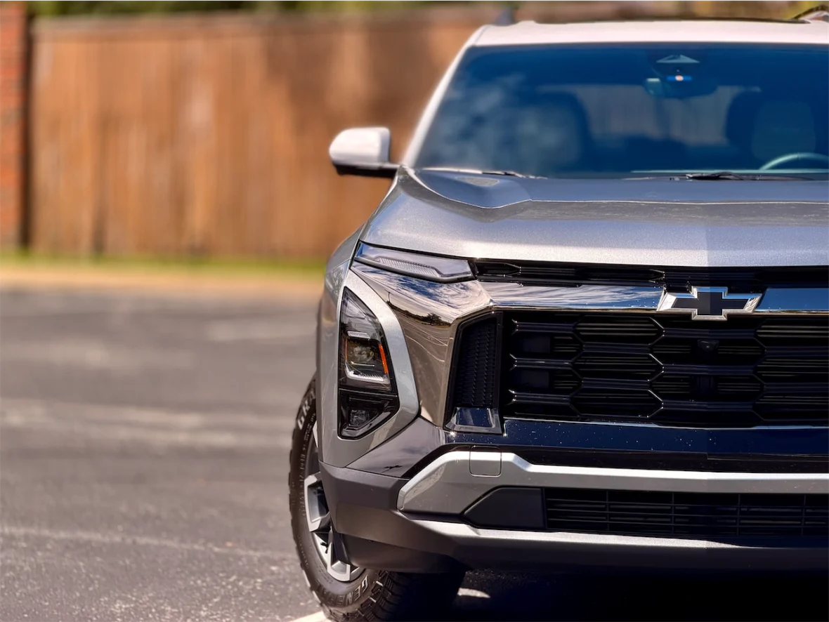 Close-up view of a silver Chevrolet SUV parked in a driveway with a wooden fence in the background.
