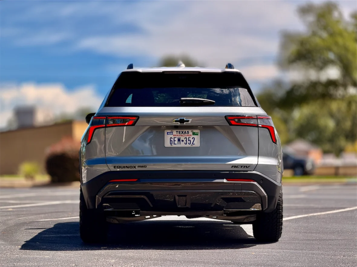 Rear view of a silver Chevrolet Equinox parked on a paved surface with blue sky and trees in the background.