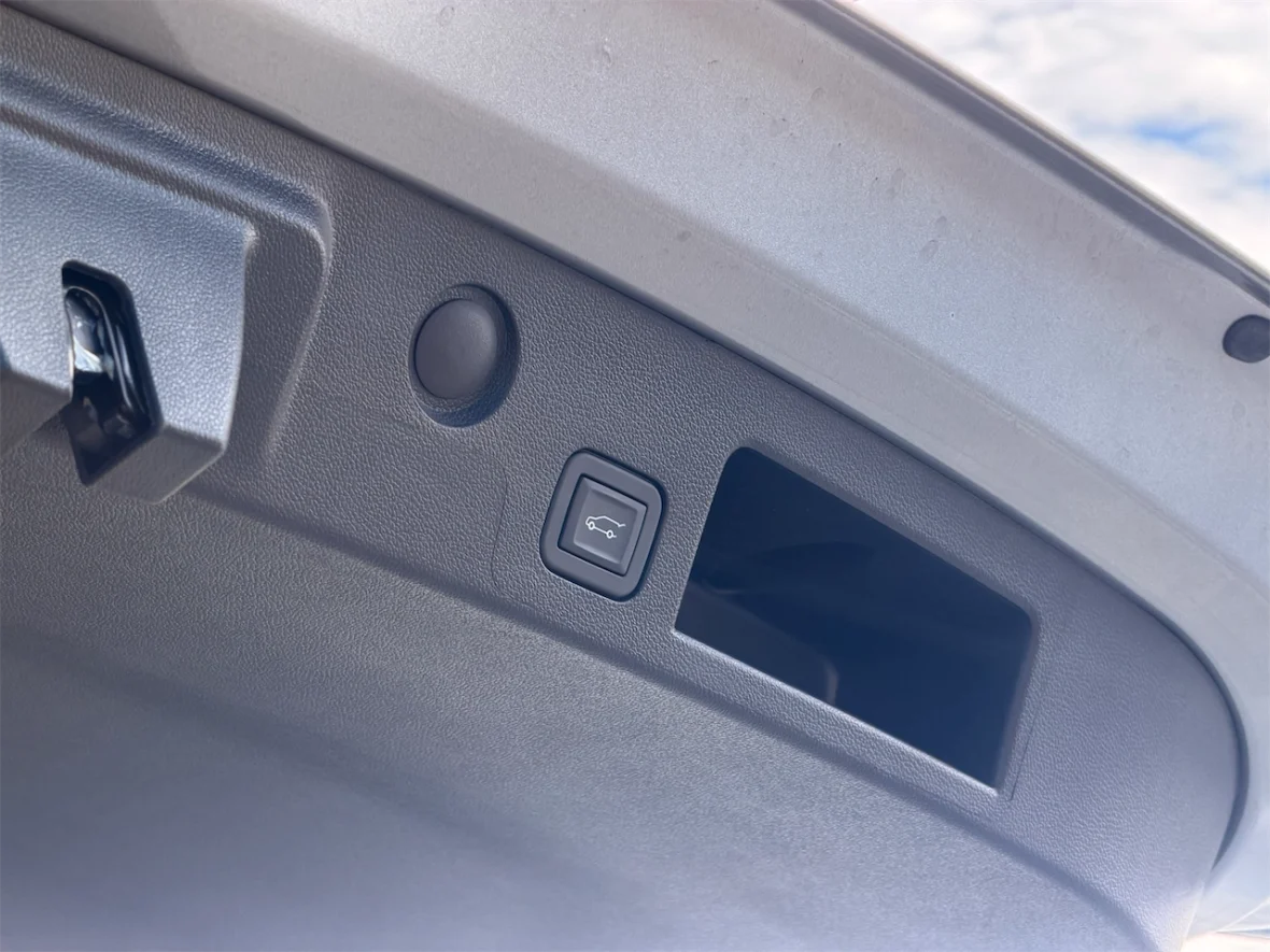 Interior view of a car trunk, showing the trunk release button and a small storage compartment.
