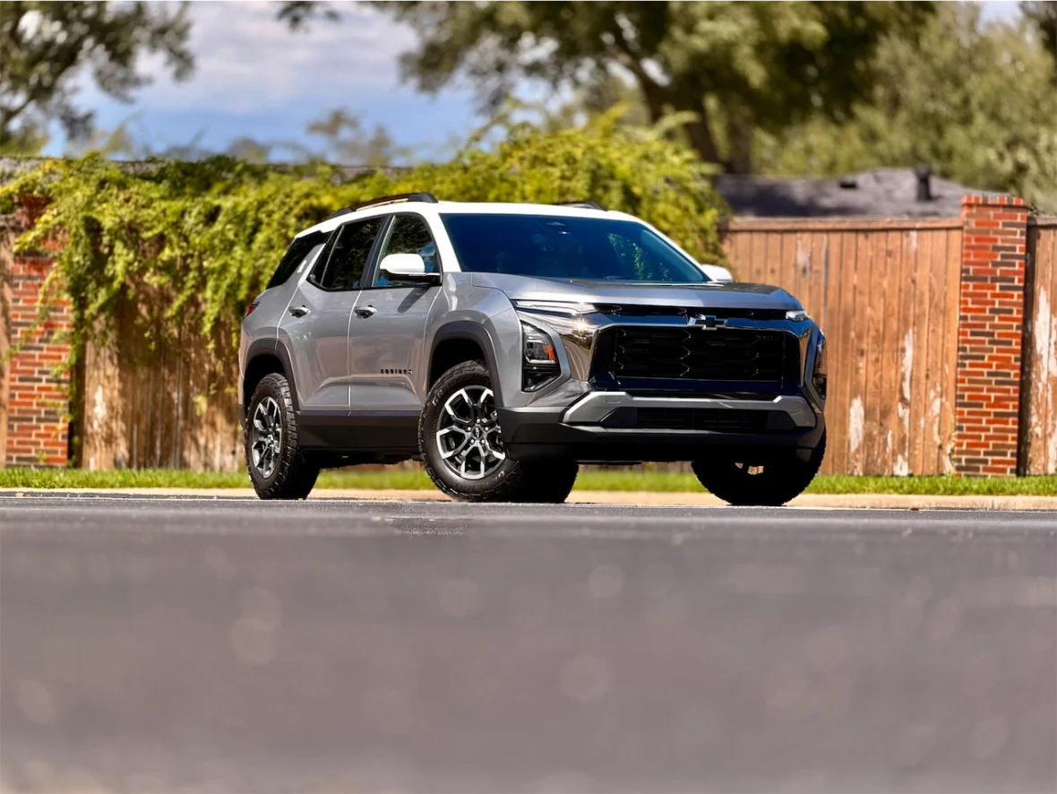 A silver Chevrolet SUV parked on a road with a blurred background of greenery and rustic wooden fences.