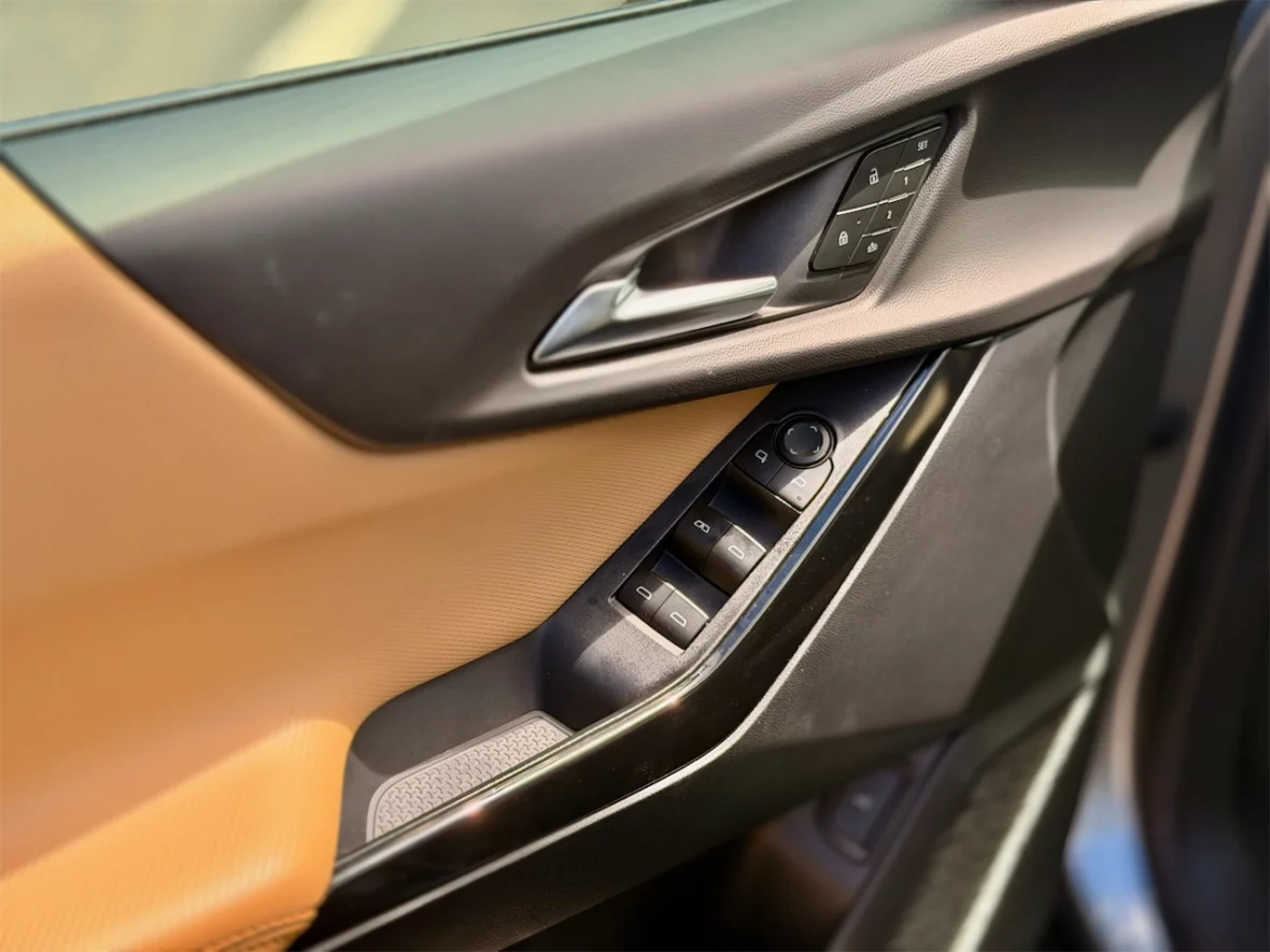 Close-up of a car door interior showing window and lock controls with a combination of black and tan materials.