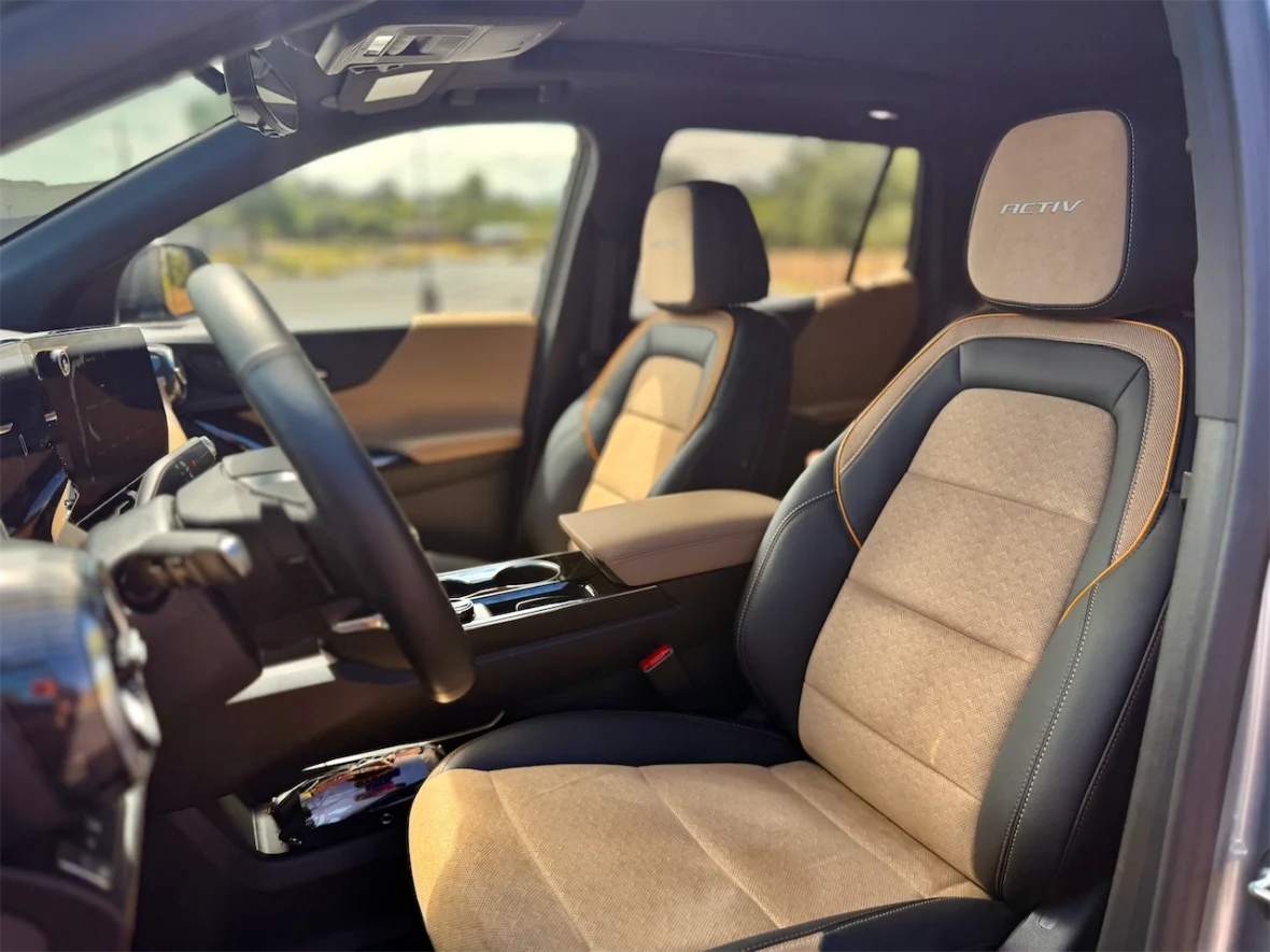 Interior view of a modern car showing tan and black seats with orange stitching, a steering wheel, and a digital dashboard.