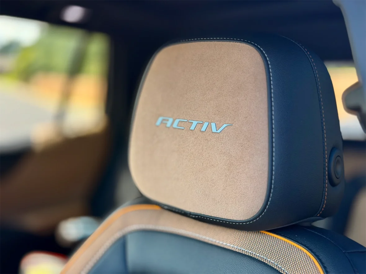 Close-up of a car headrest with the word 'ACTIV' embroidered in blue, showcasing a combination of suede-like and leather materials.