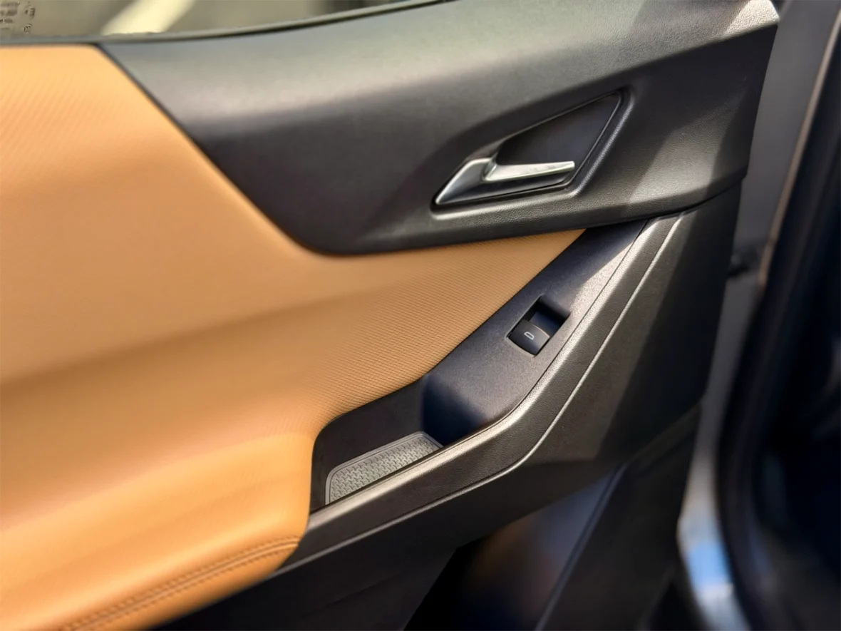 Close-up of a car door interior, featuring a combination of textured black and orange materials, with a door handle and a window control button.