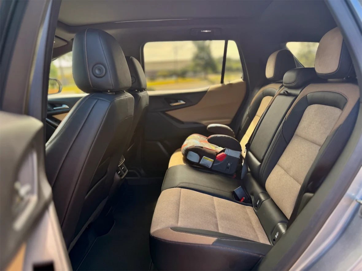 Interior view of the backseat of an SUV, featuring black and tan upholstery, with a child car seat placed in the middle.