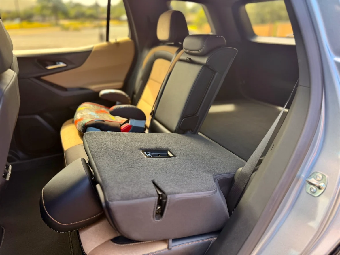 Interior view of a vehicle's backseat, showcasing a foldable armrest and a child safety seat on the seat.