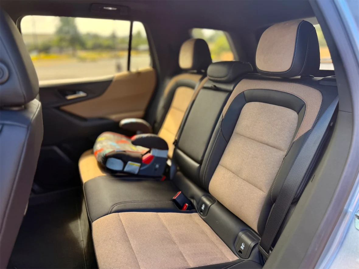 Interior view of the backseat of a car featuring two brown and black fabric seats and a child safety seat on the left.