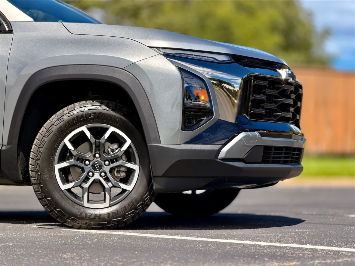 Close-up of the front wheel and grille of a gray SUV featuring alloy wheels and a rugged tire design.