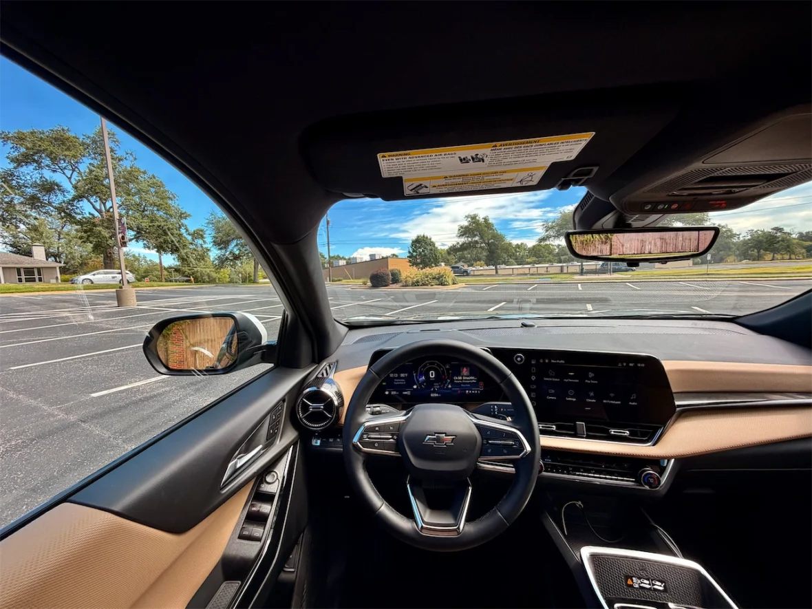 Interior view of a modern car showing the steering wheel, dashboard, and side mirror with an outdoor scene visible through the windshield.