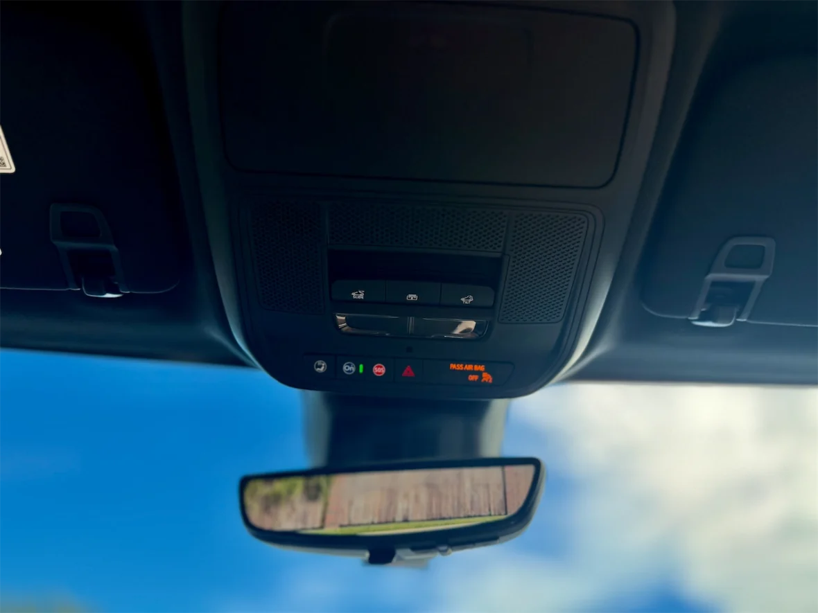 Close-up view of a car's overhead console with buttons for lights, safety features, and a rearview mirror reflecting the sky.