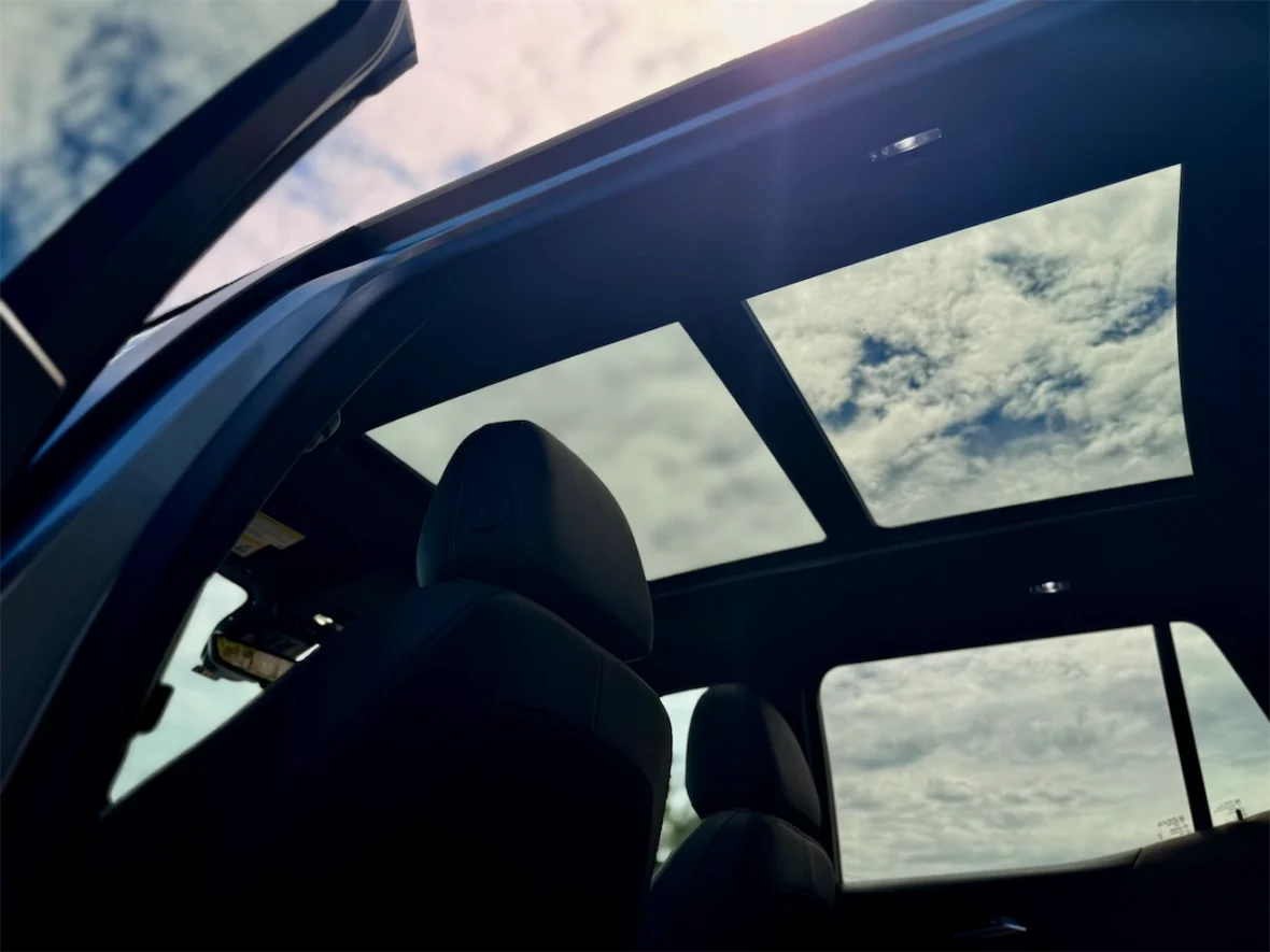Interior view of a car showcasing a panoramic sunroof and blue sky with clouds above.