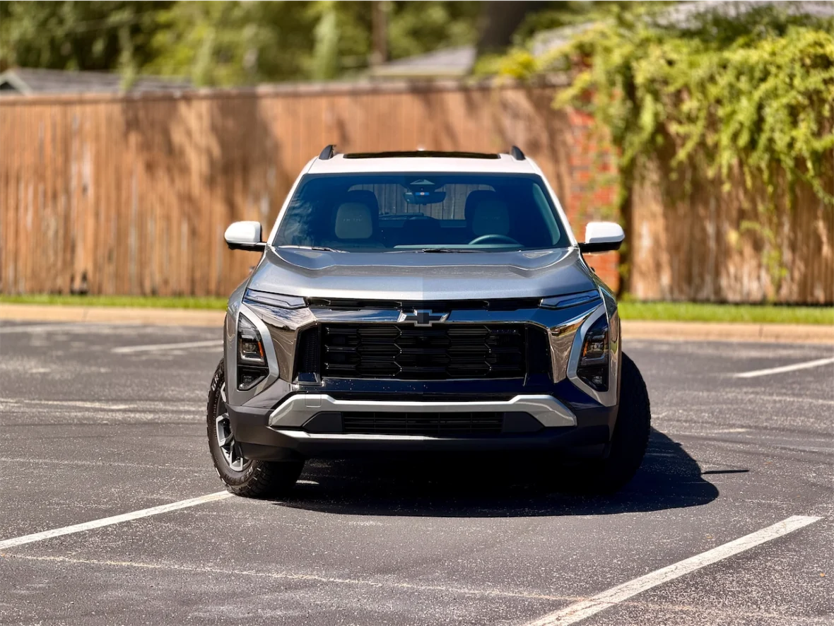 Front view of a silver and black SUV parked on a paved surface with a wooden fence in the background.