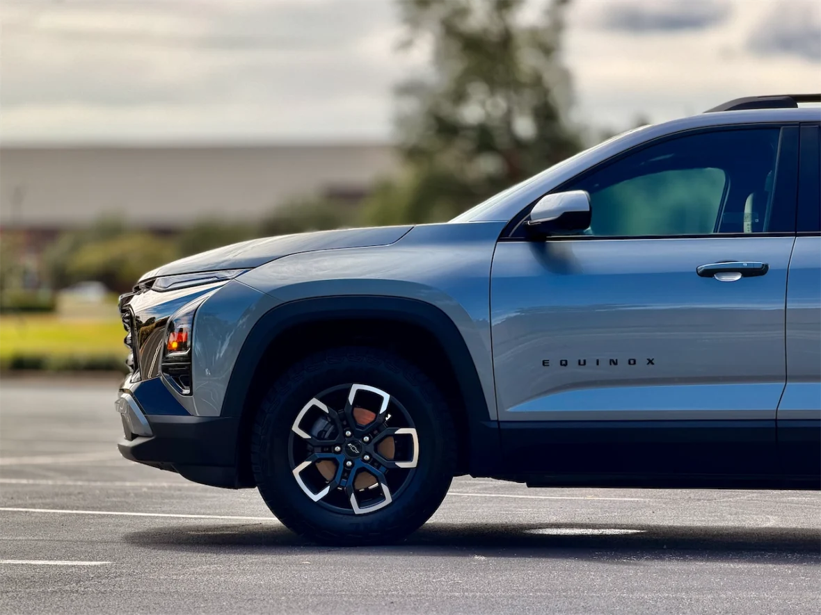 Side profile of a gray Chevrolet Equinox parked in a lot with trees and a cloudy sky in the background.