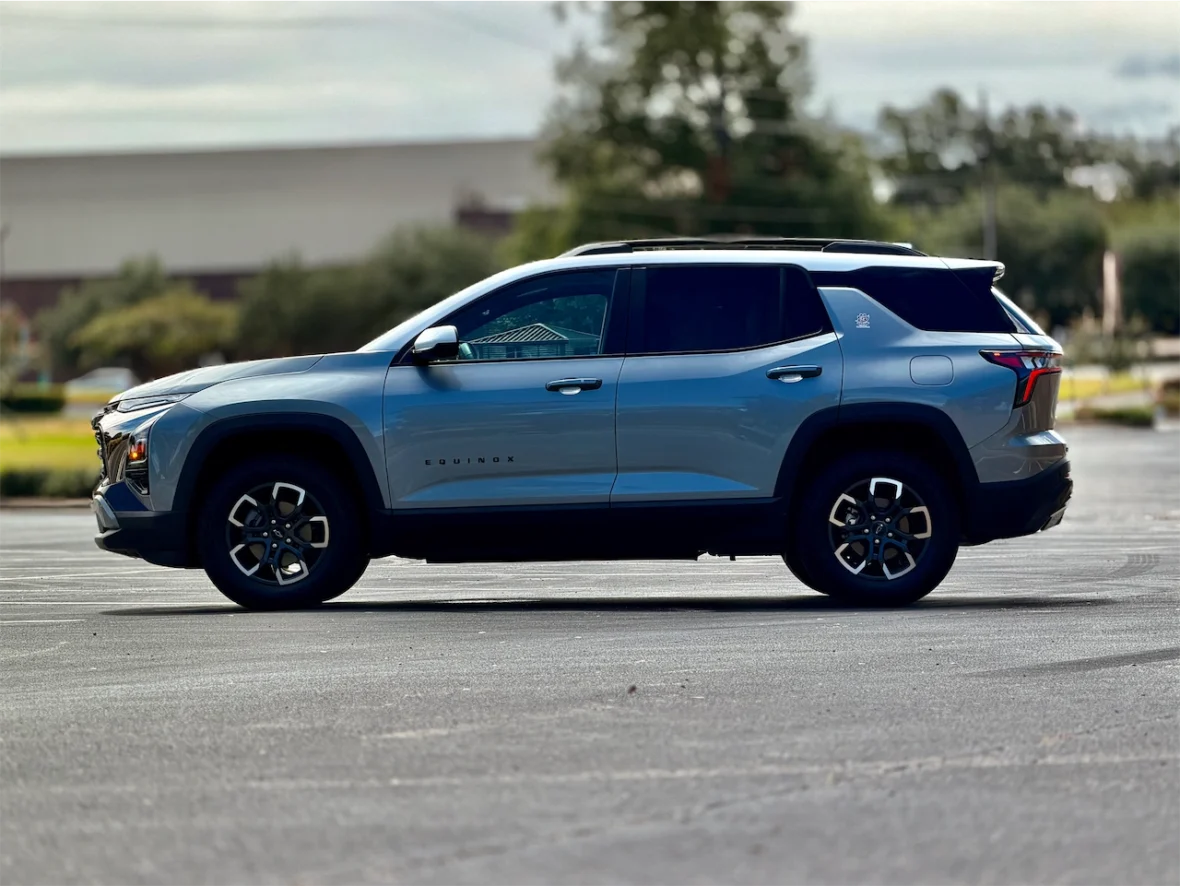 Side view of a gray Chevrolet Equinox SUV parked on a roadway with greenery in the background.