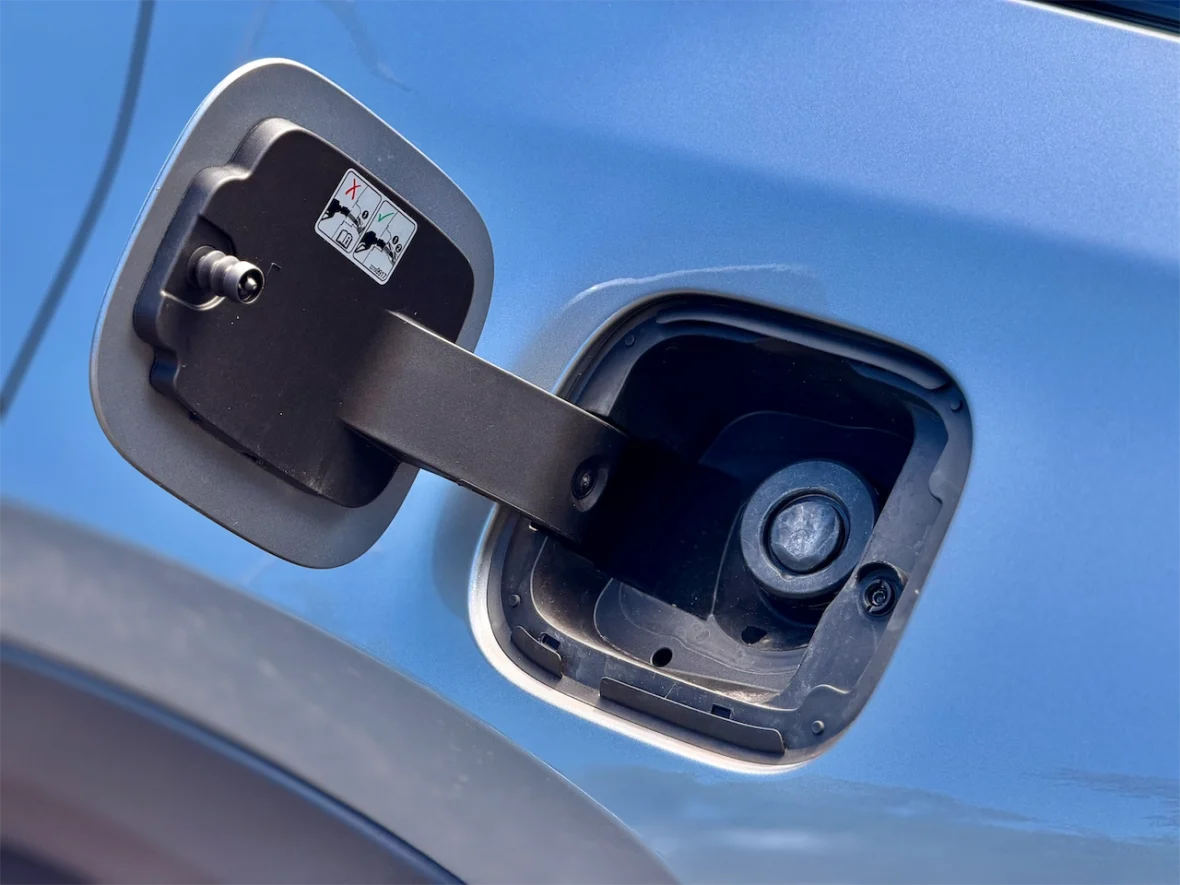 Close-up of a car fuel cap area, showing the lever mechanism and fuel inlet on a blue vehicle.