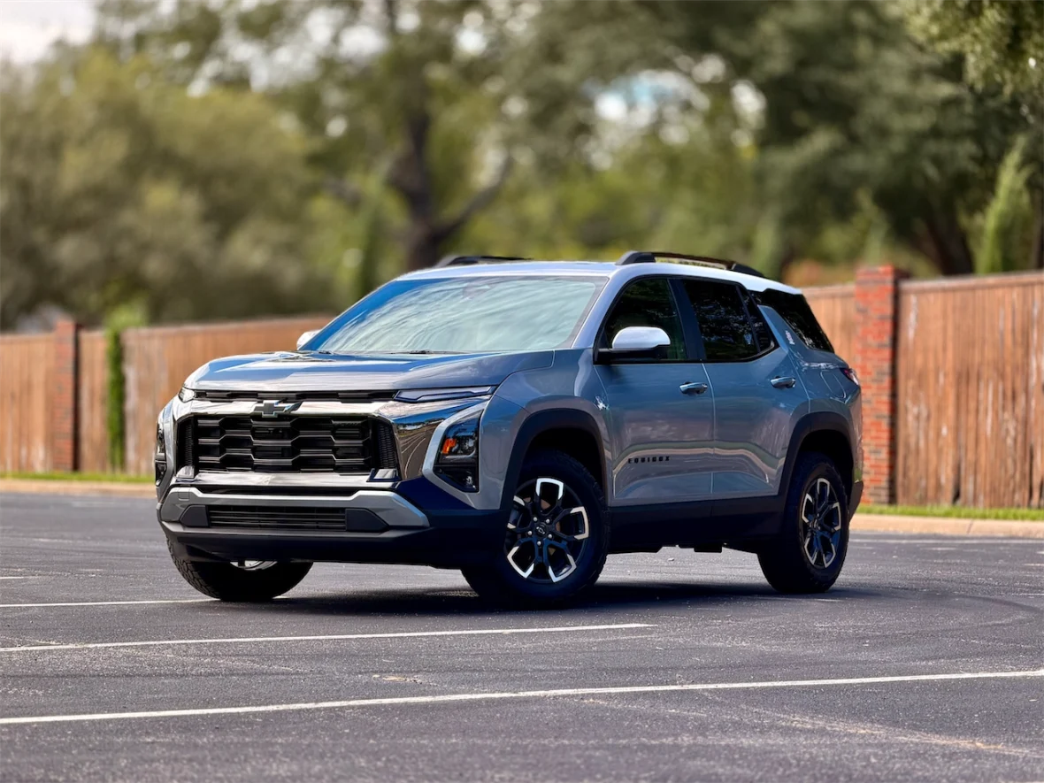 A blue Chevy SUV parked on a paved surface with trees and a wooden fence in the background.
