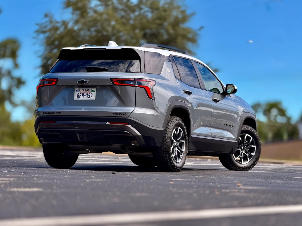A silver Chevrolet Equinox parked on a blacktop surface with trees in the background under a blue sky.
