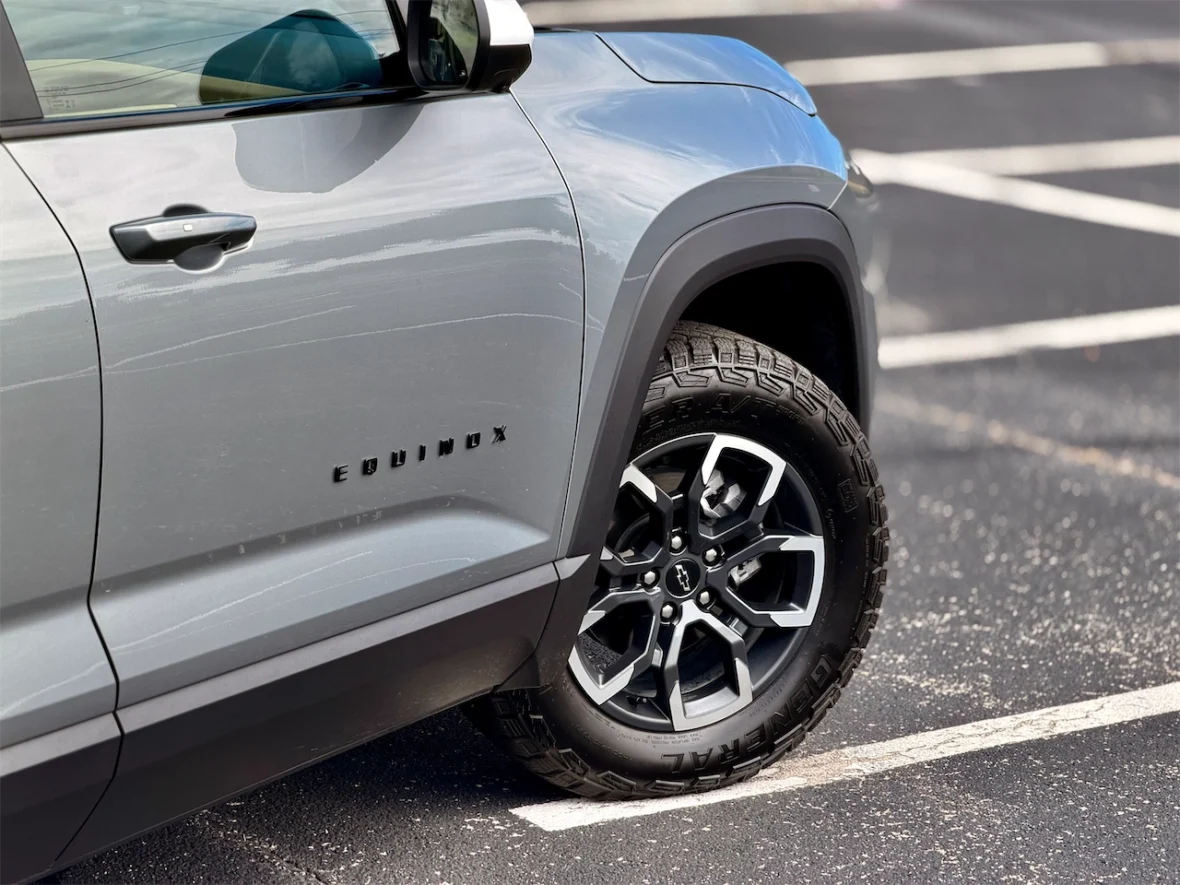Close-up of a gray Chevrolet Equinox showing the driver's side door and wheel, with a focus on the logo and tire tread pattern.