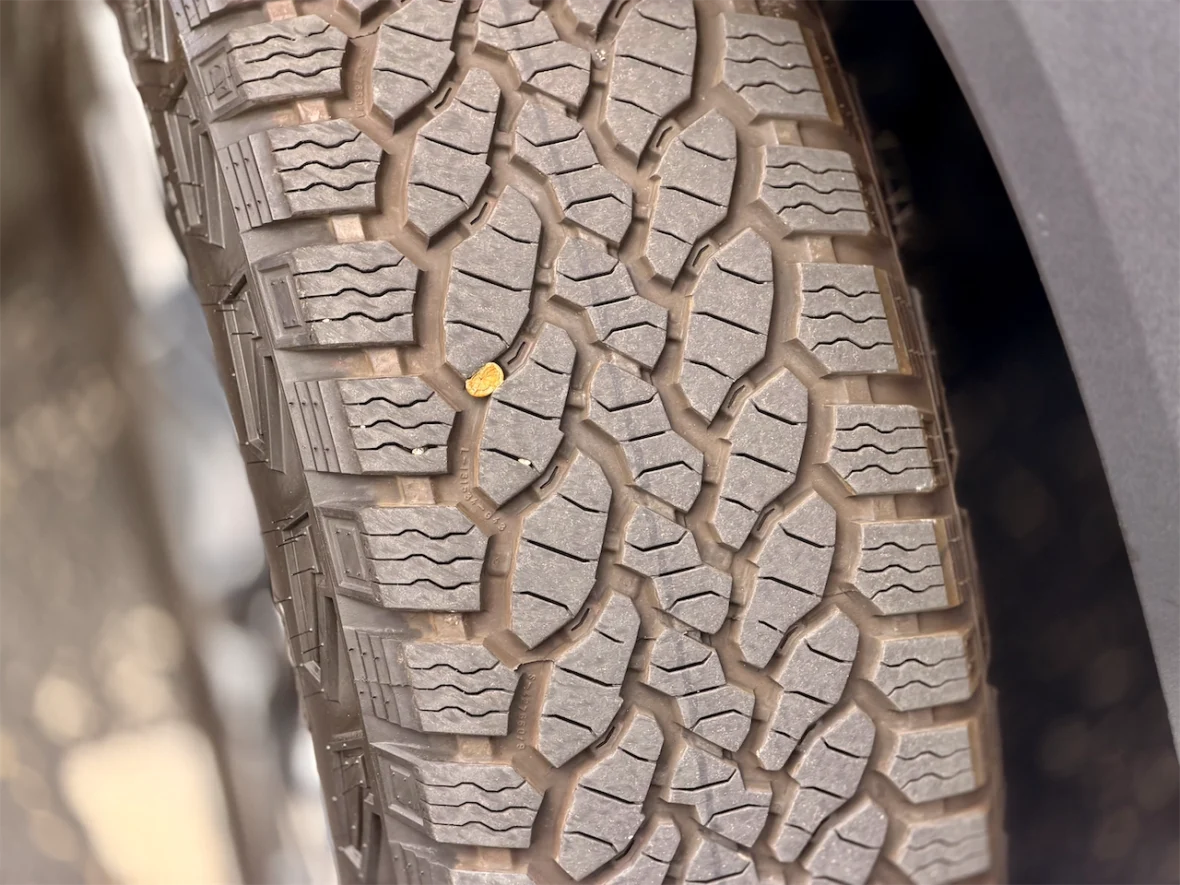 Close-up of a vehicle tire showing detailed tread patterns and a small piece of debris embedded in the grooves.