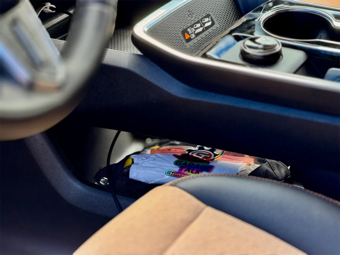 Close-up of a car's center console showing the gear shift area, cup holders, and a bag labeled 'Garage Talk' tucked underneath.