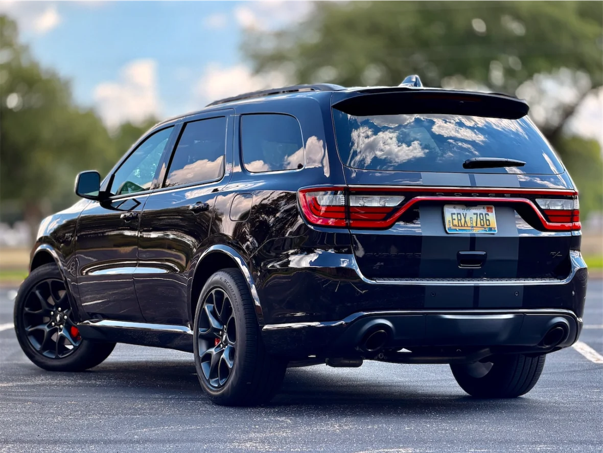 A black SUV parked in a lot, showing its rear and side profile, with a clear blue sky and greenery in the background.