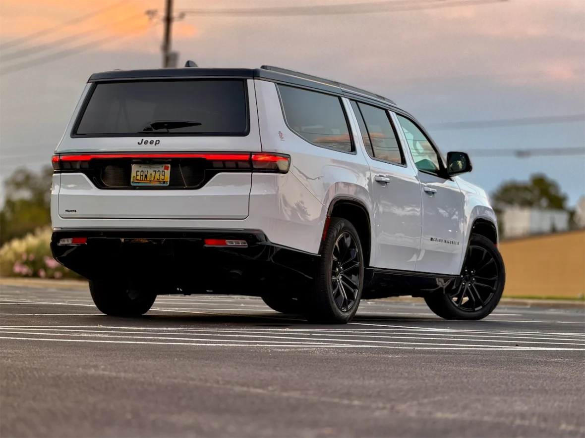 The 2026 Jeep Grand Wagoneer L parked in a lot with a blurred background during sunset, showcasing its modern design and black wheels.