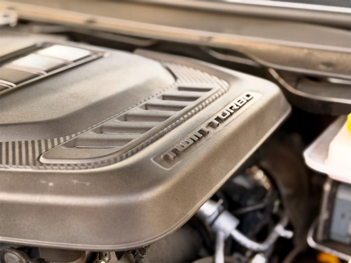 Close-up of a car engine cover with 'Twin Turbo' label, showcasing a metallic finish and design details.