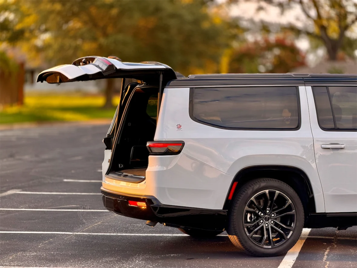 A modern SUV with an open rear hatch, parked in an empty parking lot with trees in the background.